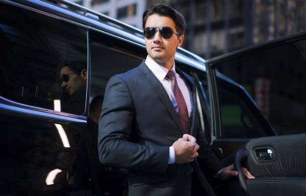 Elegancko ubrany mężczyzna w okularach przeciwsłonecznych wysiadający z samochodu